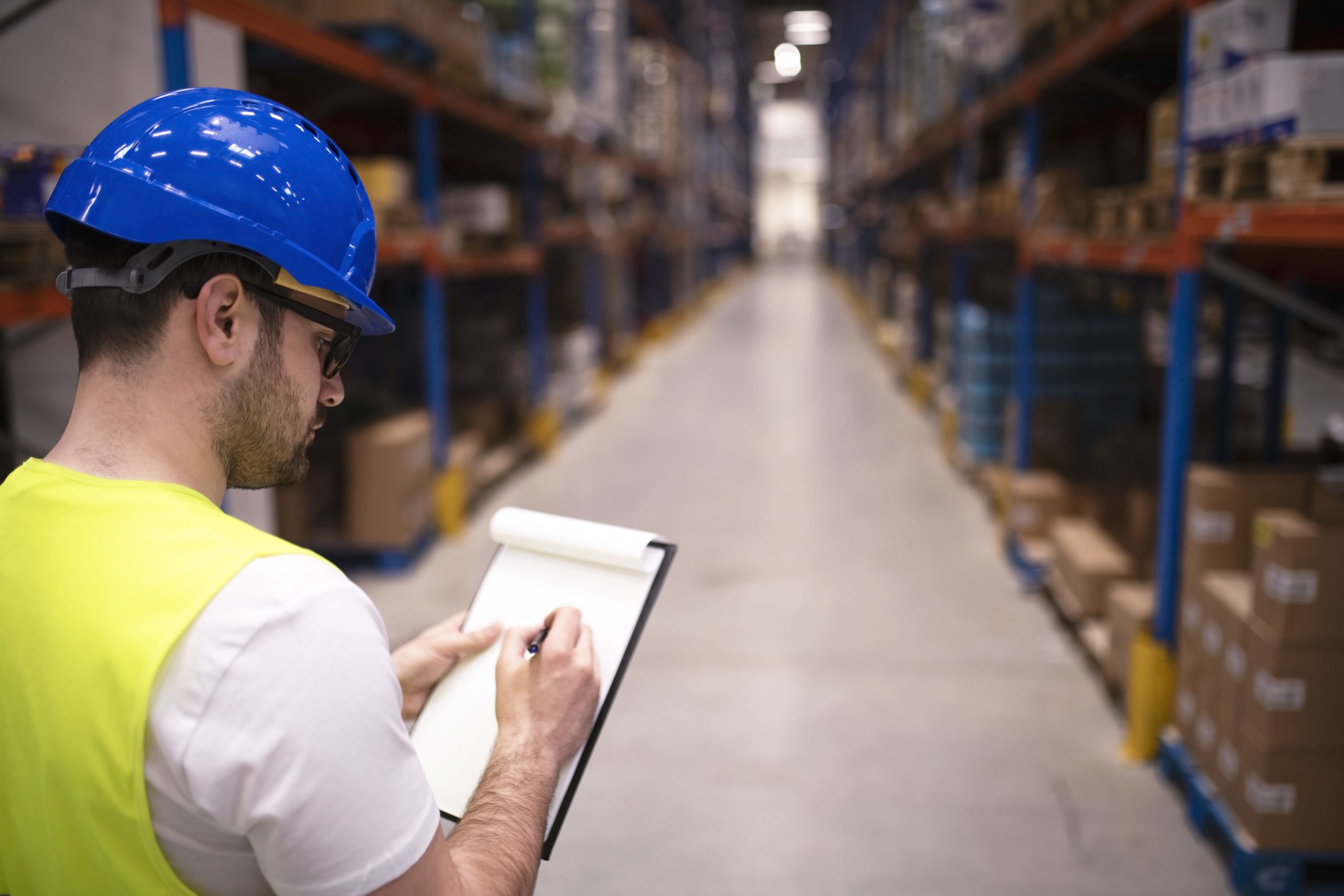 Ouvrier prenant des notes dans un hangar, casque de sécurité bleu